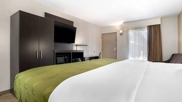 Habitación de hotel con una cama grande, televisor montado en la pared, minibar y una ventana con cortinas.