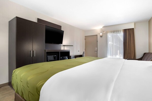 A hotel room with a large bed, a TV mounted on the wall, a minibar, and a window with curtains.