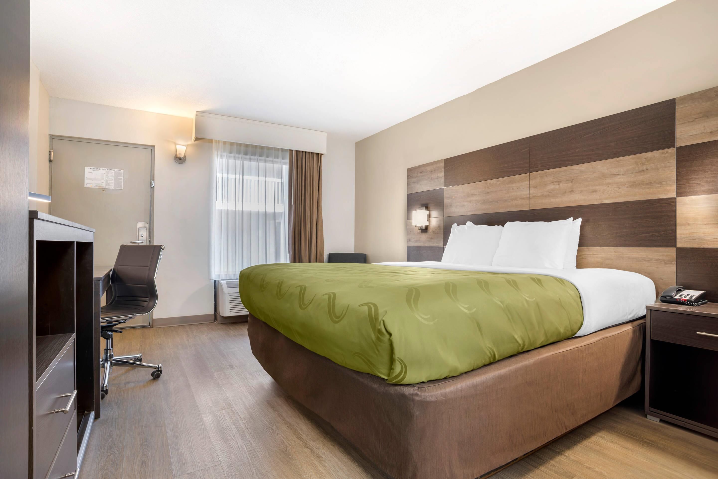 A hotel room with a large bed, a desk, a chair, and a wardrobe.