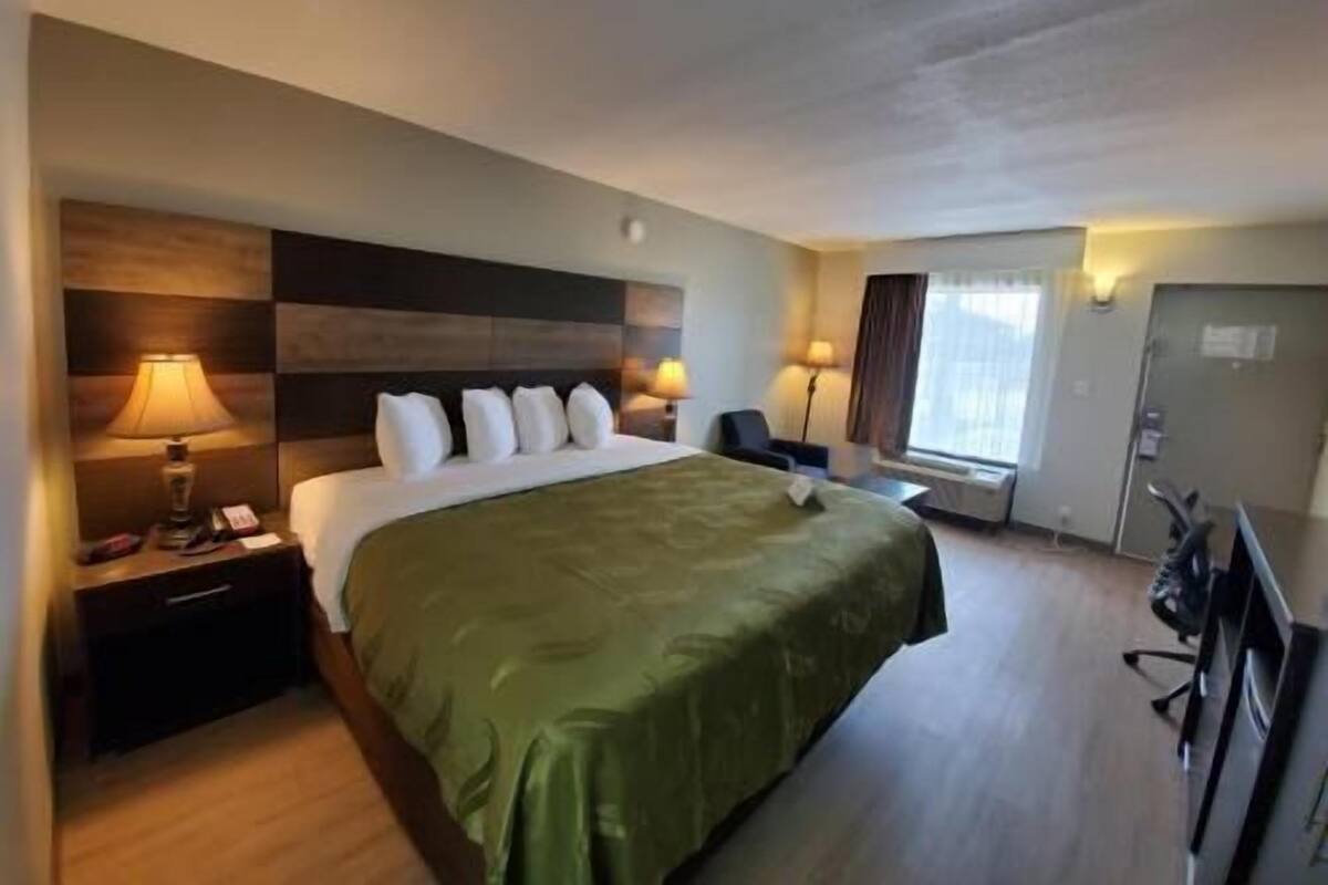 Una camera d'albergo con un letto, lampade sui comodini, una scrivania, una sedia e una televisione.