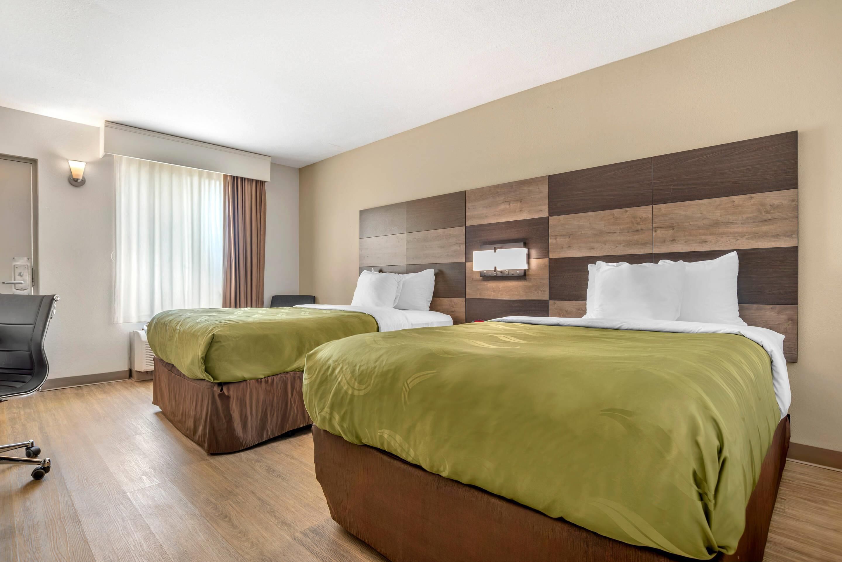 A hotel room with two beds, a desk, and a chair.