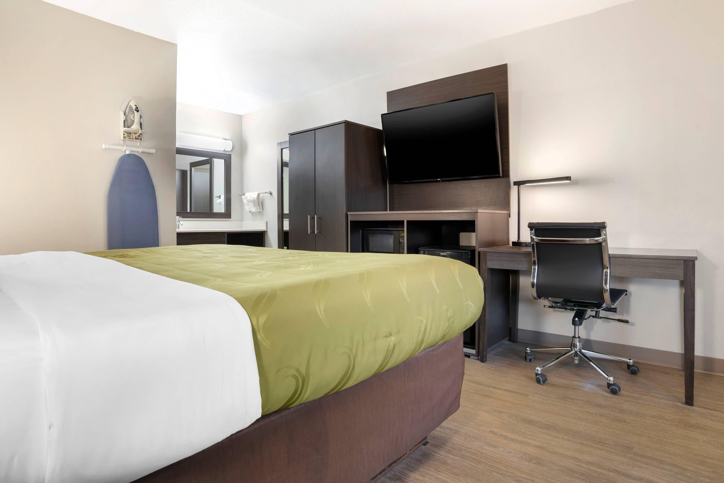 A hotel room with a bed, a desk, a chair, a TV, and a wardrobe.