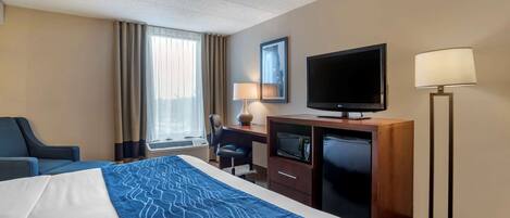 A hotel room with a large bed, a desk with a television, a desk lamp, and a chair.