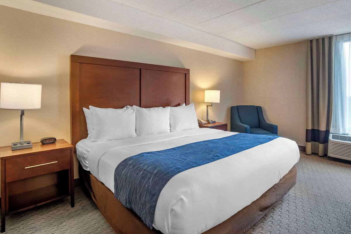 A hotel room with a large bed, two bedside tables, a chair, and a window with curtains.