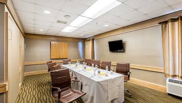A conference room with a long table, chairs, a flat-screen TV, and an air conditioning unit.