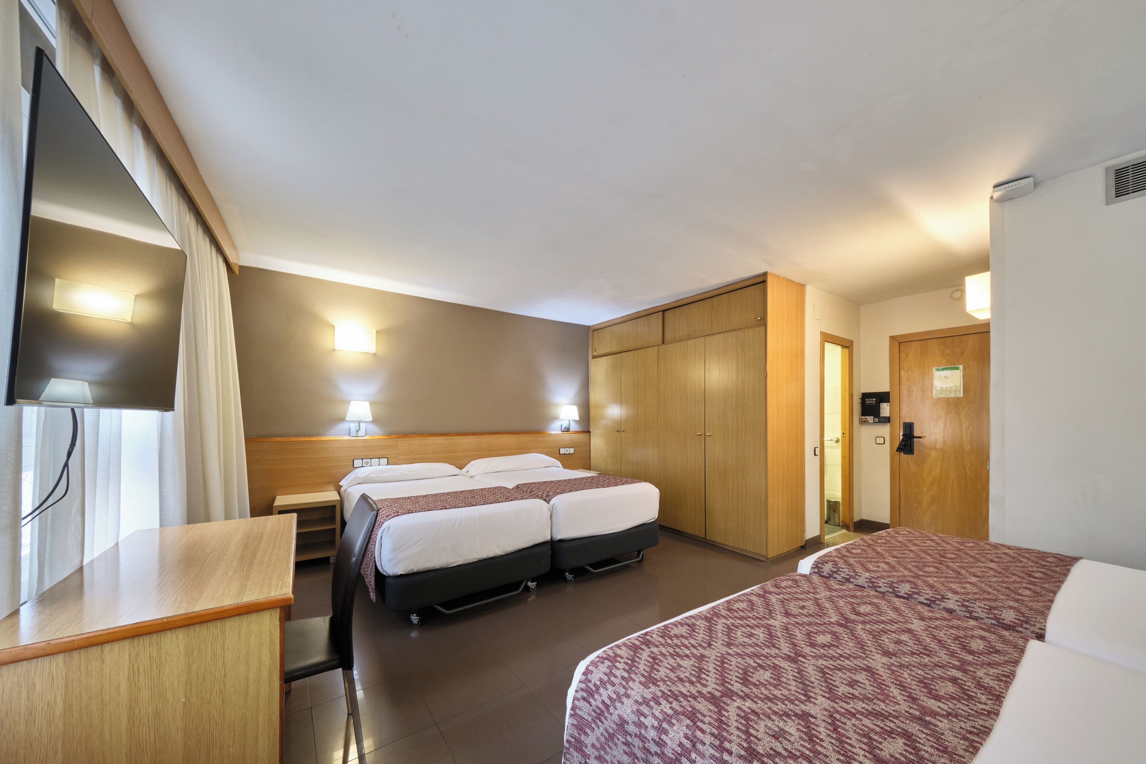 Ein Hotelzimmer mit zwei Betten, einem Schreibtisch, einem Kleiderschrank und einem Fernseher.