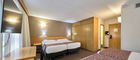 Ein Hotelzimmer mit zwei Betten, einem Schreibtisch, einem Kleiderschrank und einem Fernseher.
