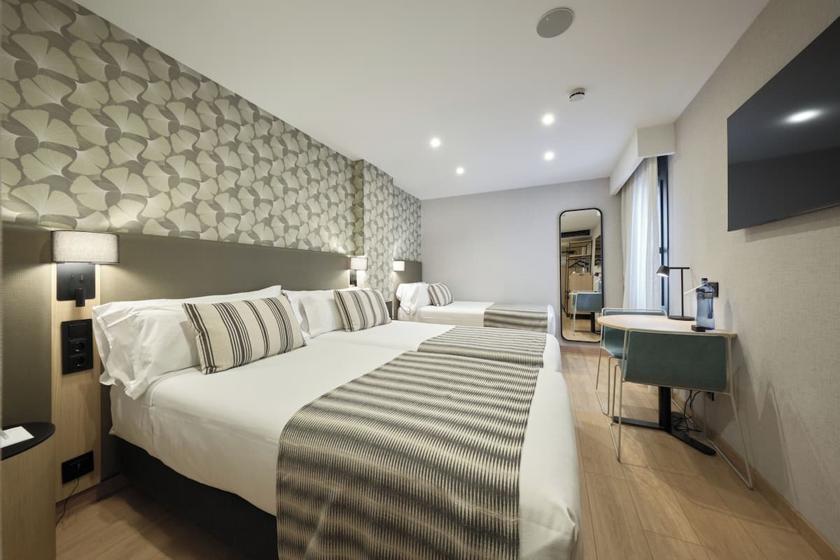 A hotel room with two beds, a desk, a chair, a TV, and a mirror.