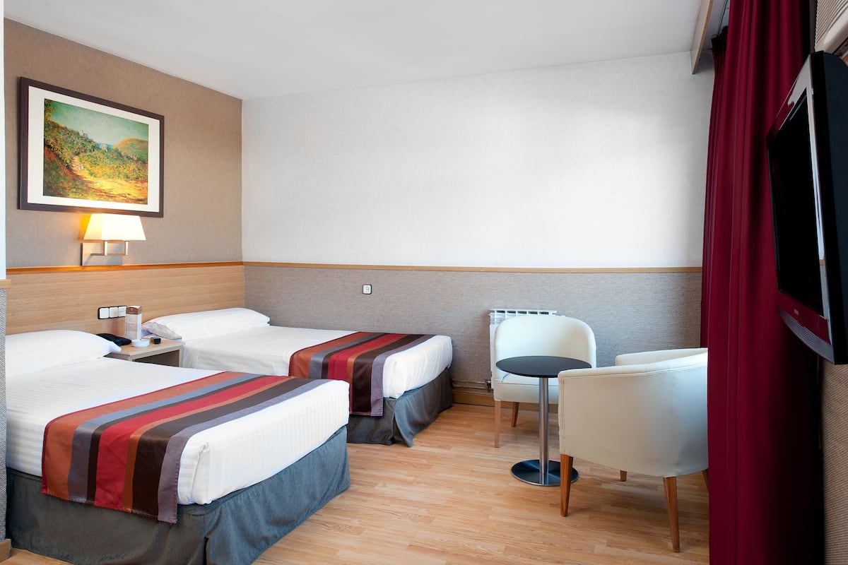 Een hotelkamer met twee bedden, een tafeltje, een stoel, een televisie en een schilderij aan de muur.