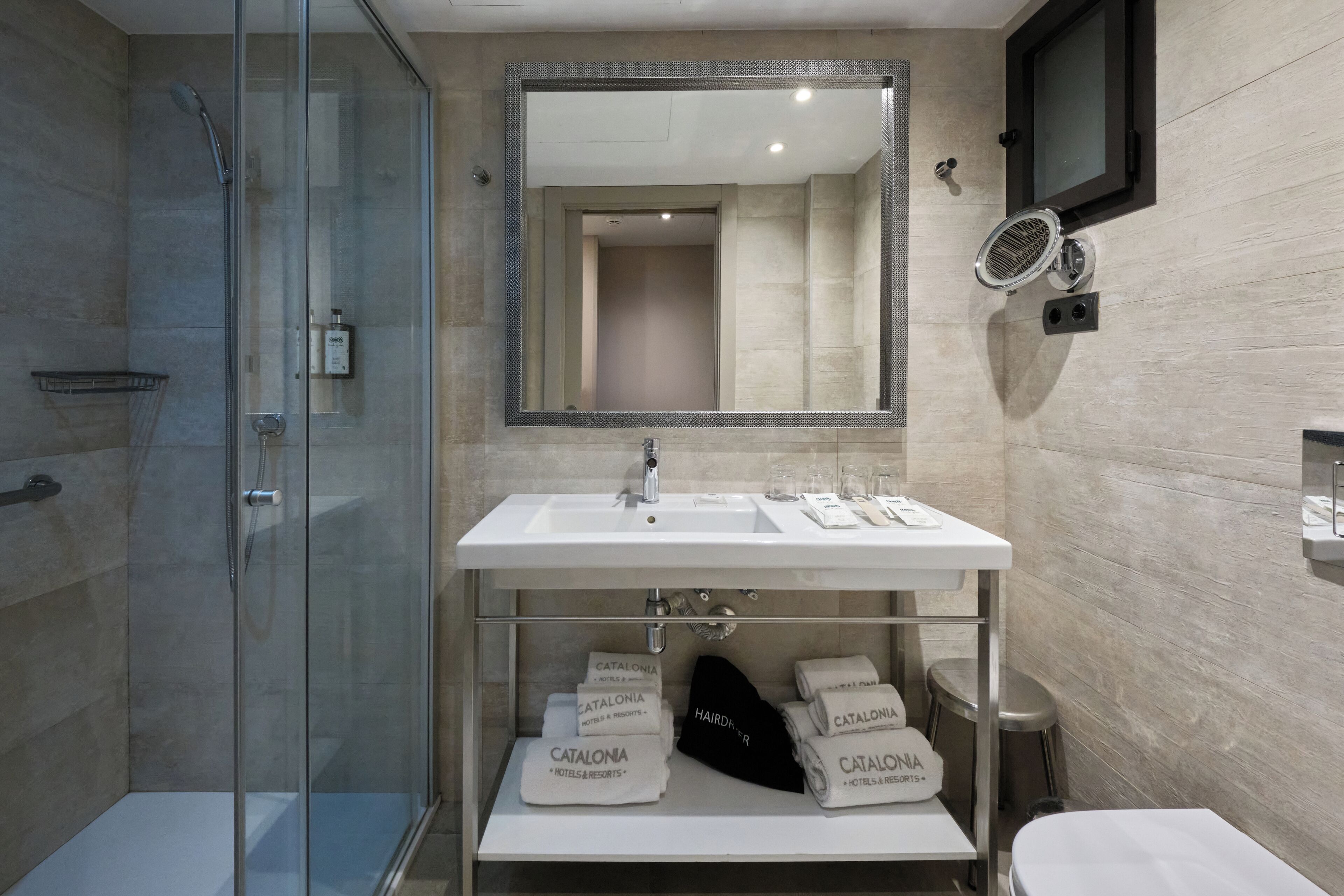 A modern bathroom with a glass-enclosed shower, a large mirror, and a sink with toiletries.