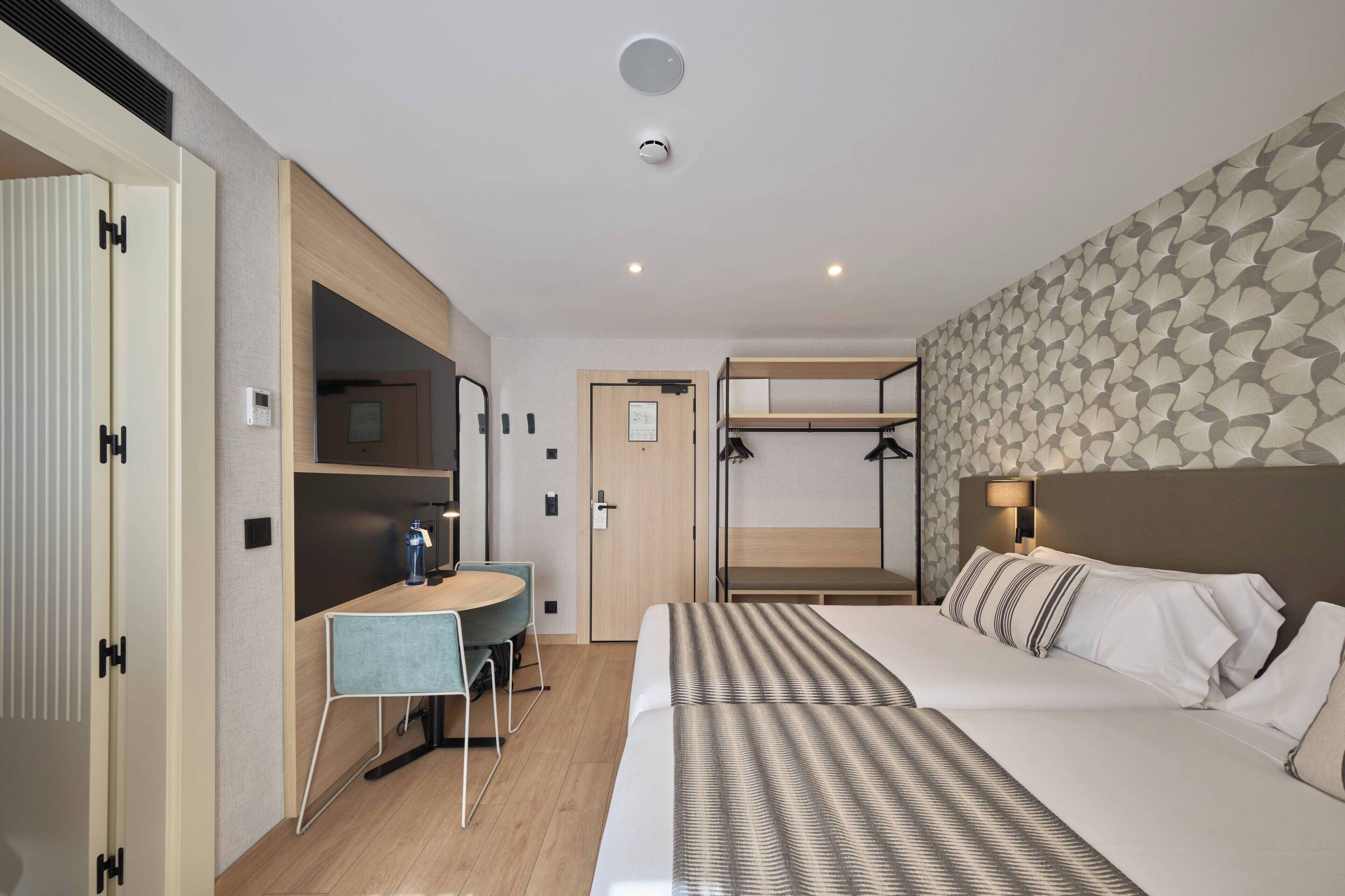 A hotel room with a bunk bed, a desk with a chair, a small table, and a bedside lamp.