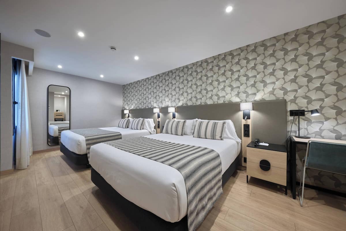 A hotel room with two beds, a desk, a chair, a nightstand, and a mirror.