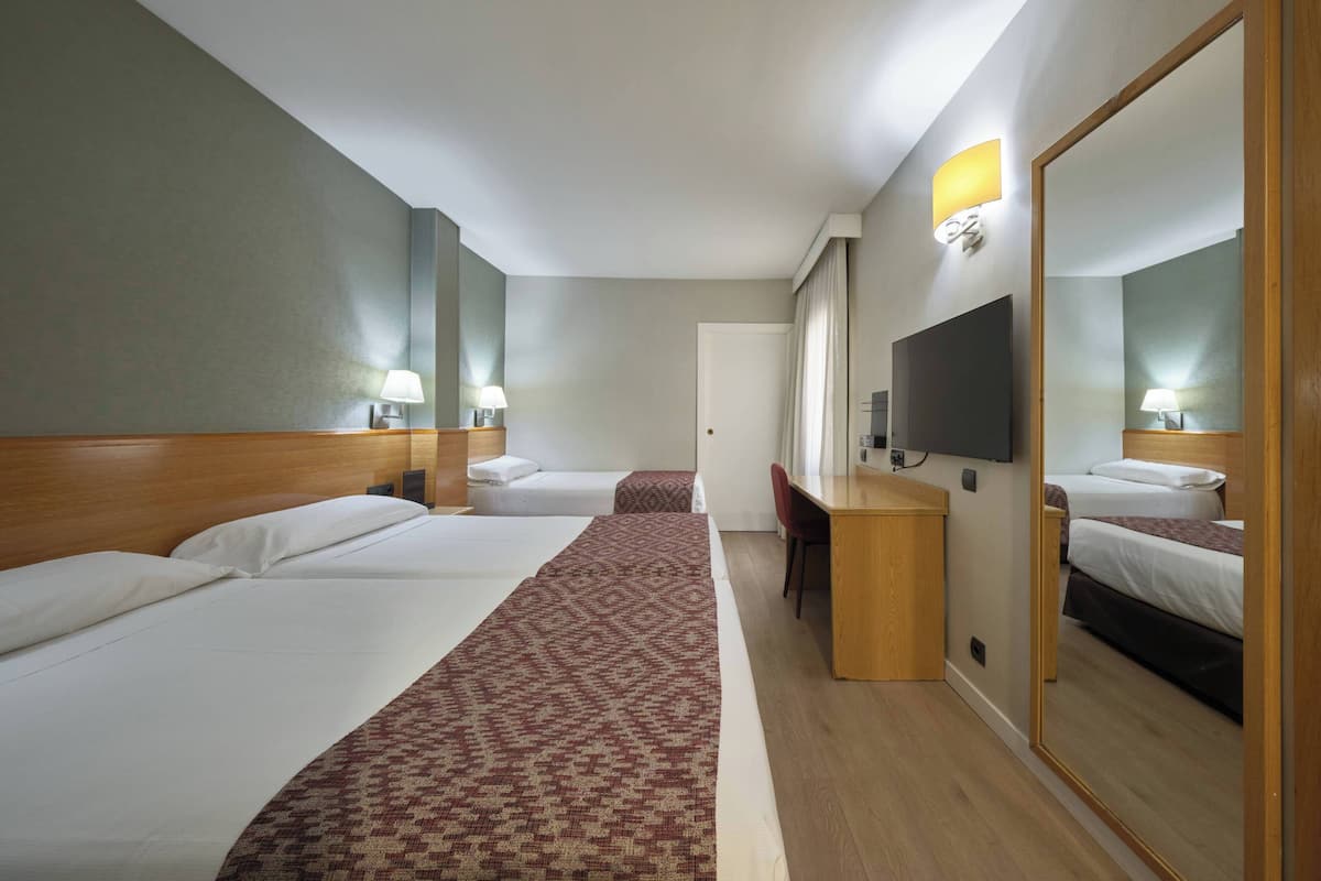 A hotel room with two beds, a desk, a chair, a TV, and a large mirror.