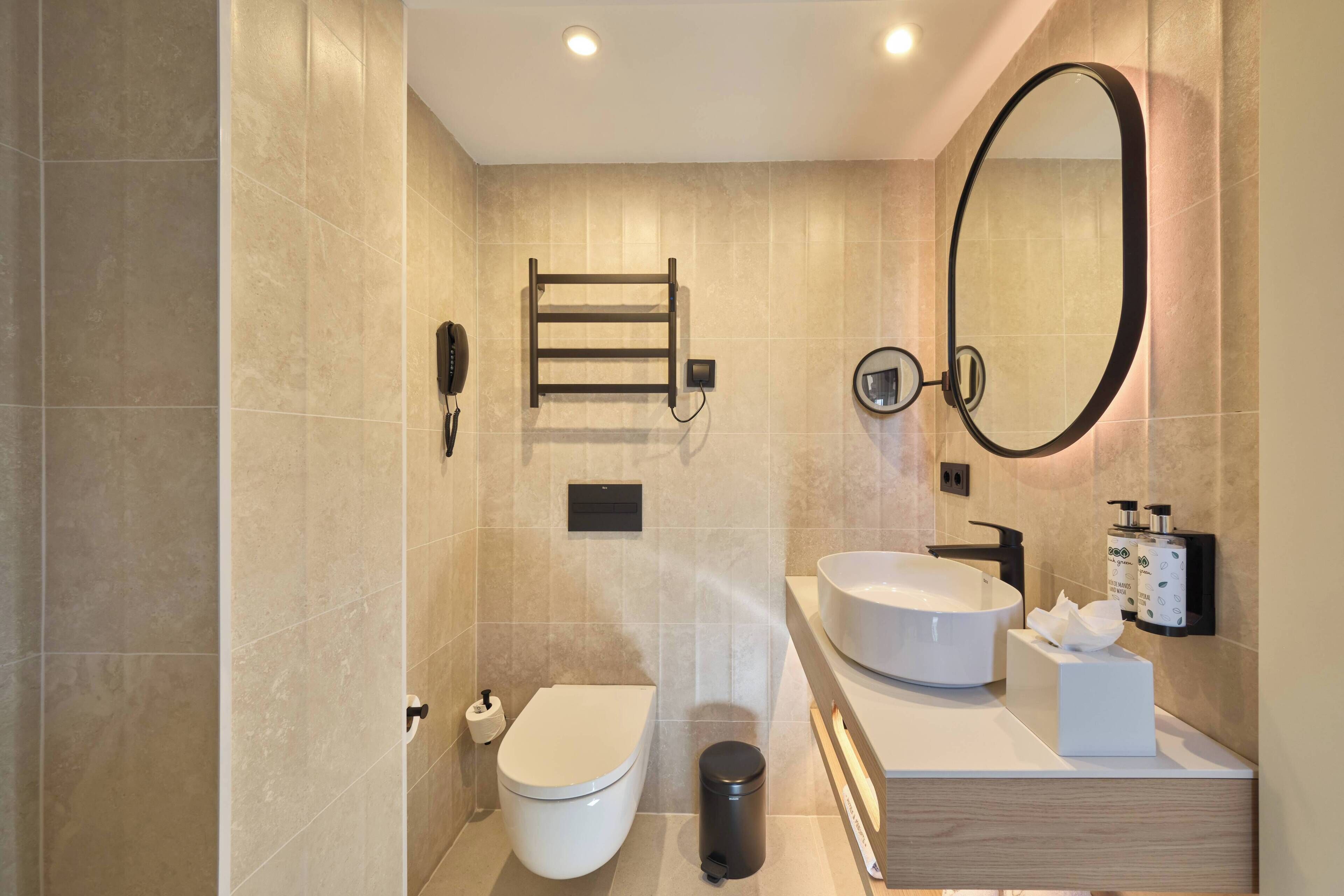 A modern bathroom with a toilet, bidet, vanity with a sink, mirror, and towel rack.