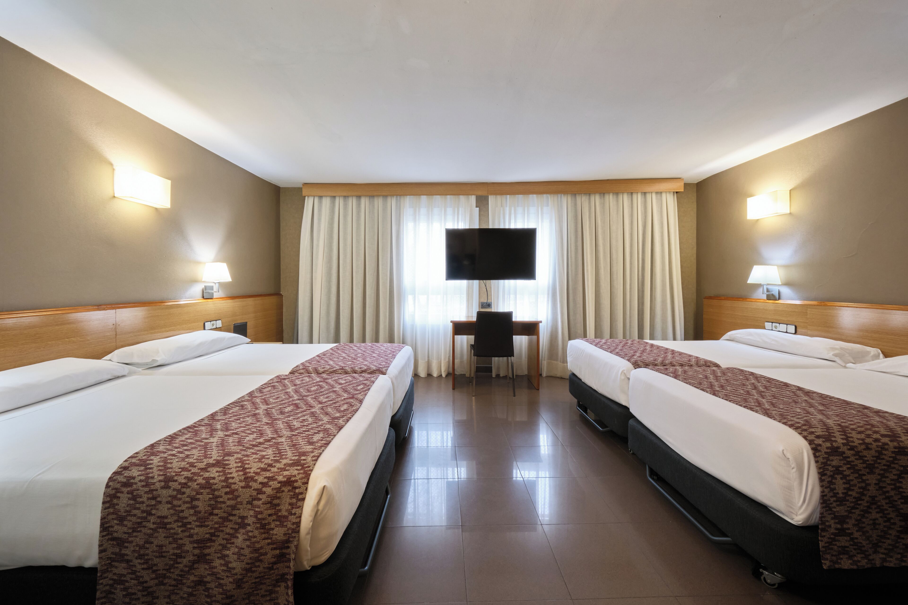 Una habitación de hotel con dos camas, un escritorio, un televisor y una ventana con cortinas.