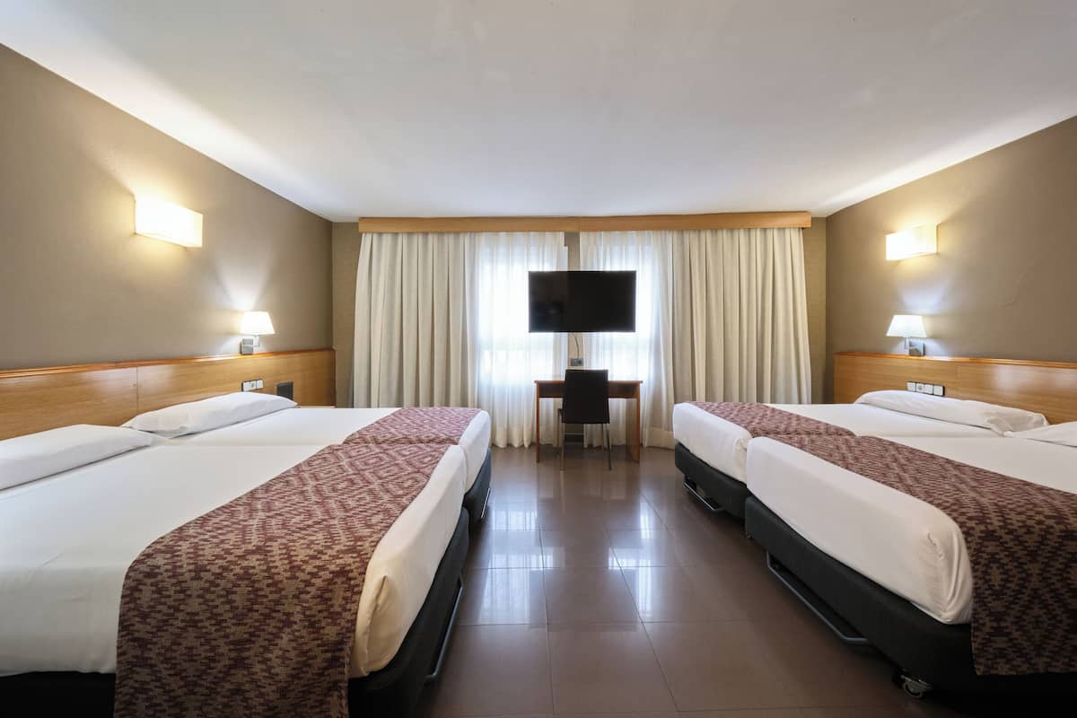 A hotel room with two beds, a desk, a TV, and a window with curtains.