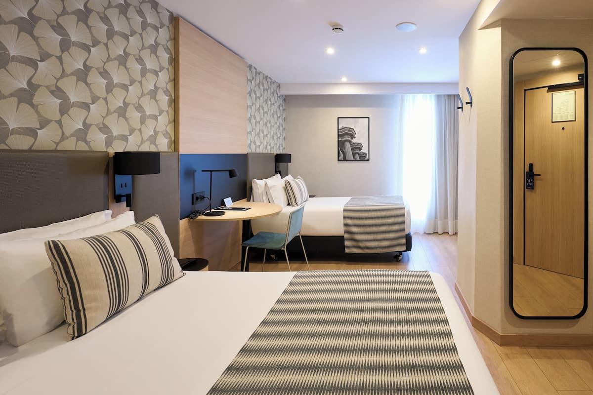 A hotel room with a bed, a desk, a chair, a small table, and a door.