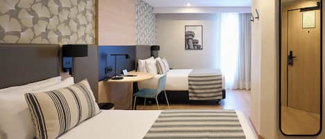 Habitación de hotel con cama, escritorio, silla, una mesita y una puerta.