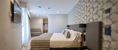 A modern hotel room with a large bed, a flat-screen TV mounted on the wall, a bedside table with a lamp, and a patterned wall.