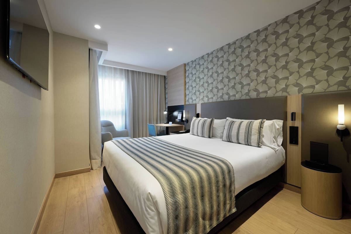 A modern hotel room with a large bed, a desk, and a television.