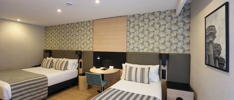 A hotel room with two beds, a desk, a chair, a small table, and a nightstand.