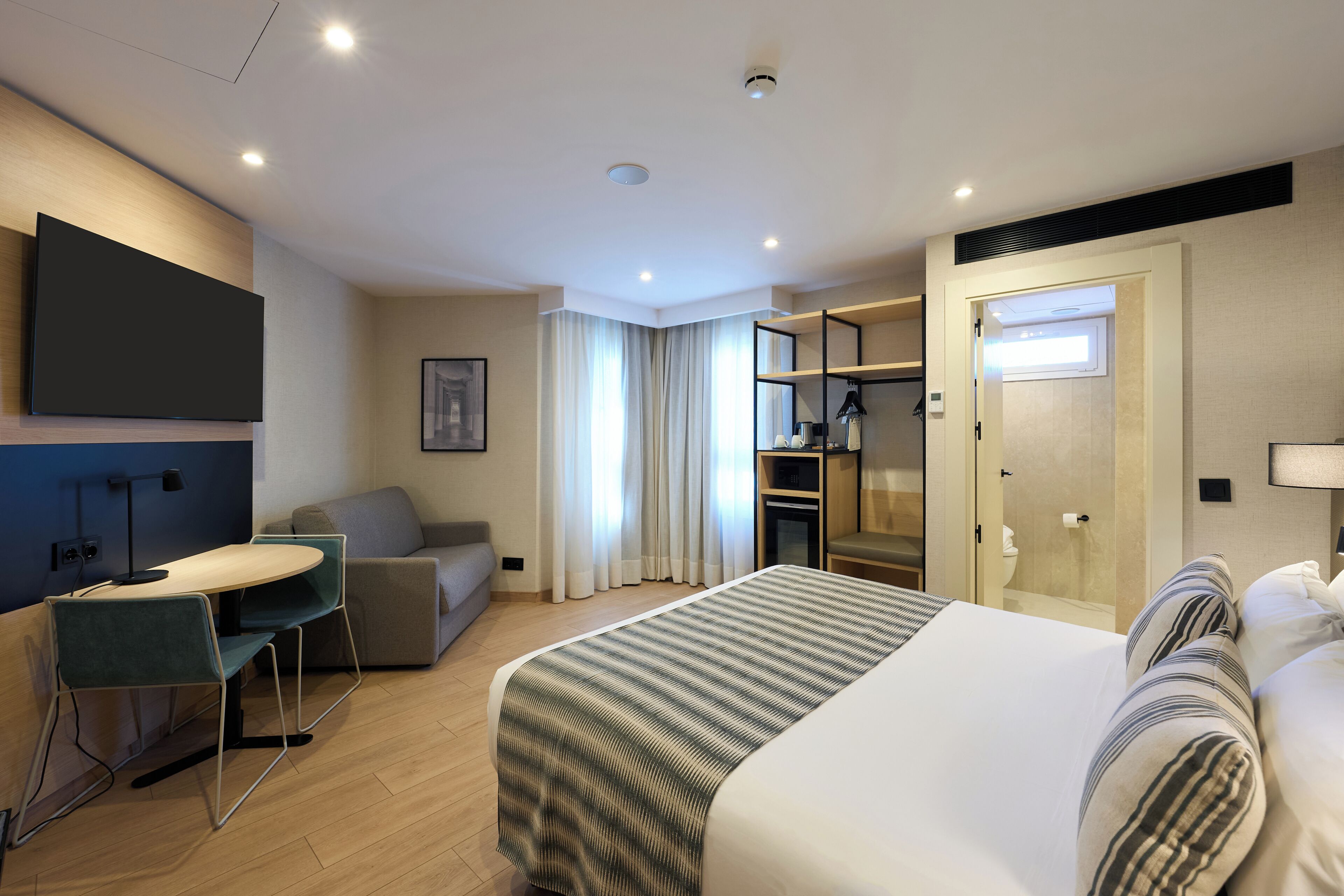 A hotel room with a bed, a desk with chairs, a sofa, a wardrobe, and a bathroom.