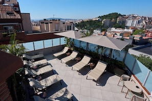 A rooftop terrace with sun loungers, a table, and a large umbrella.