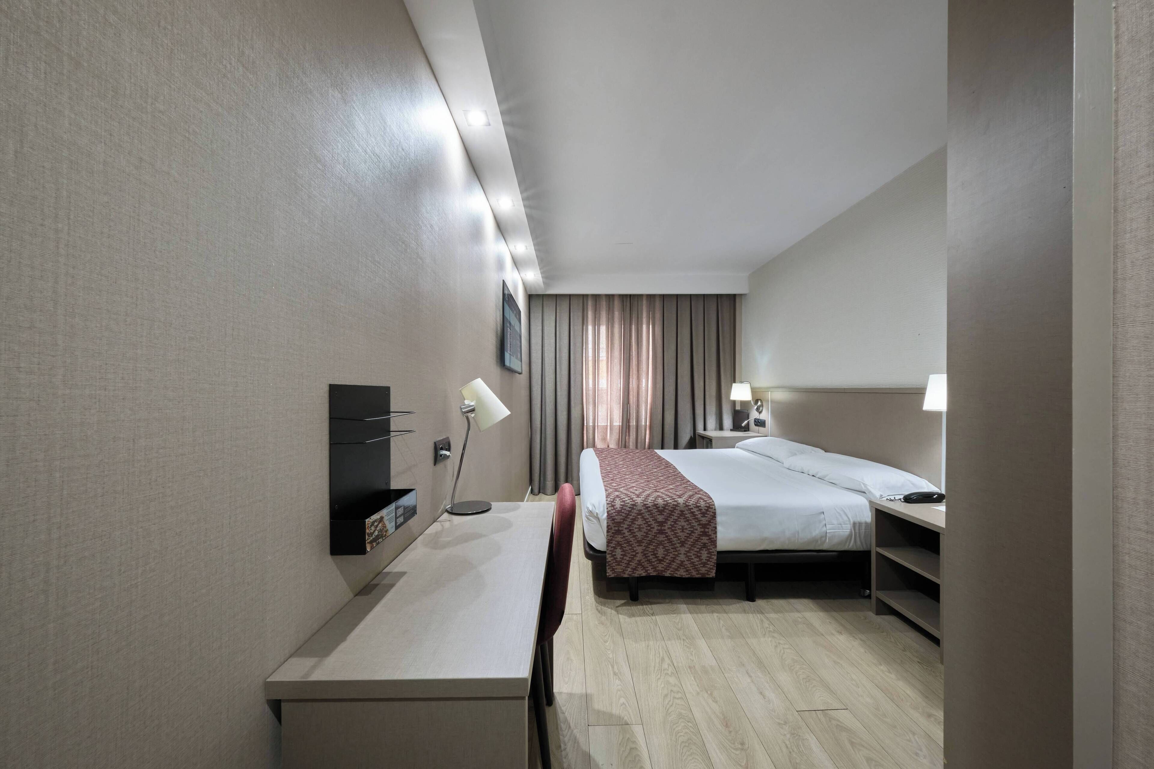 A hotel room with a bed, desk, chair, and bedside lamps.