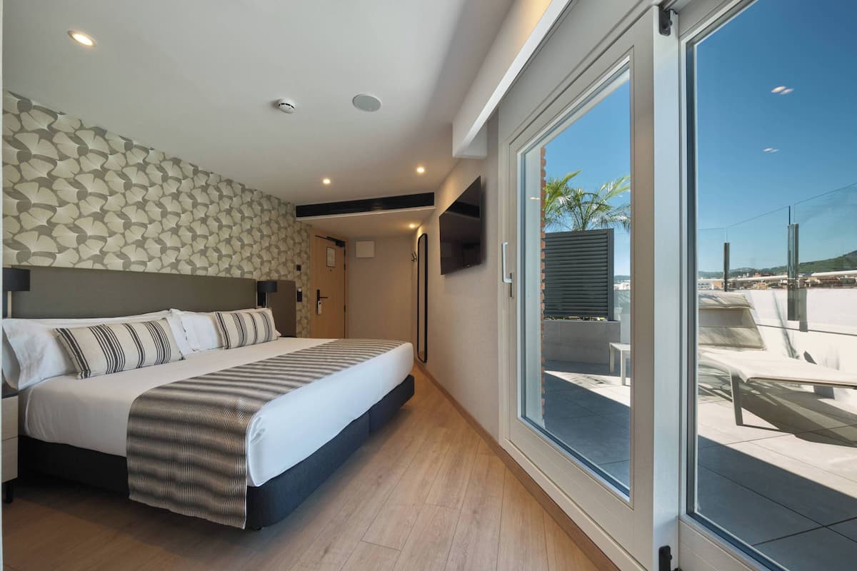 A modern bedroom with a large bed, a patterned headboard, a TV, and a sliding glass door leading to an outdoor area.
