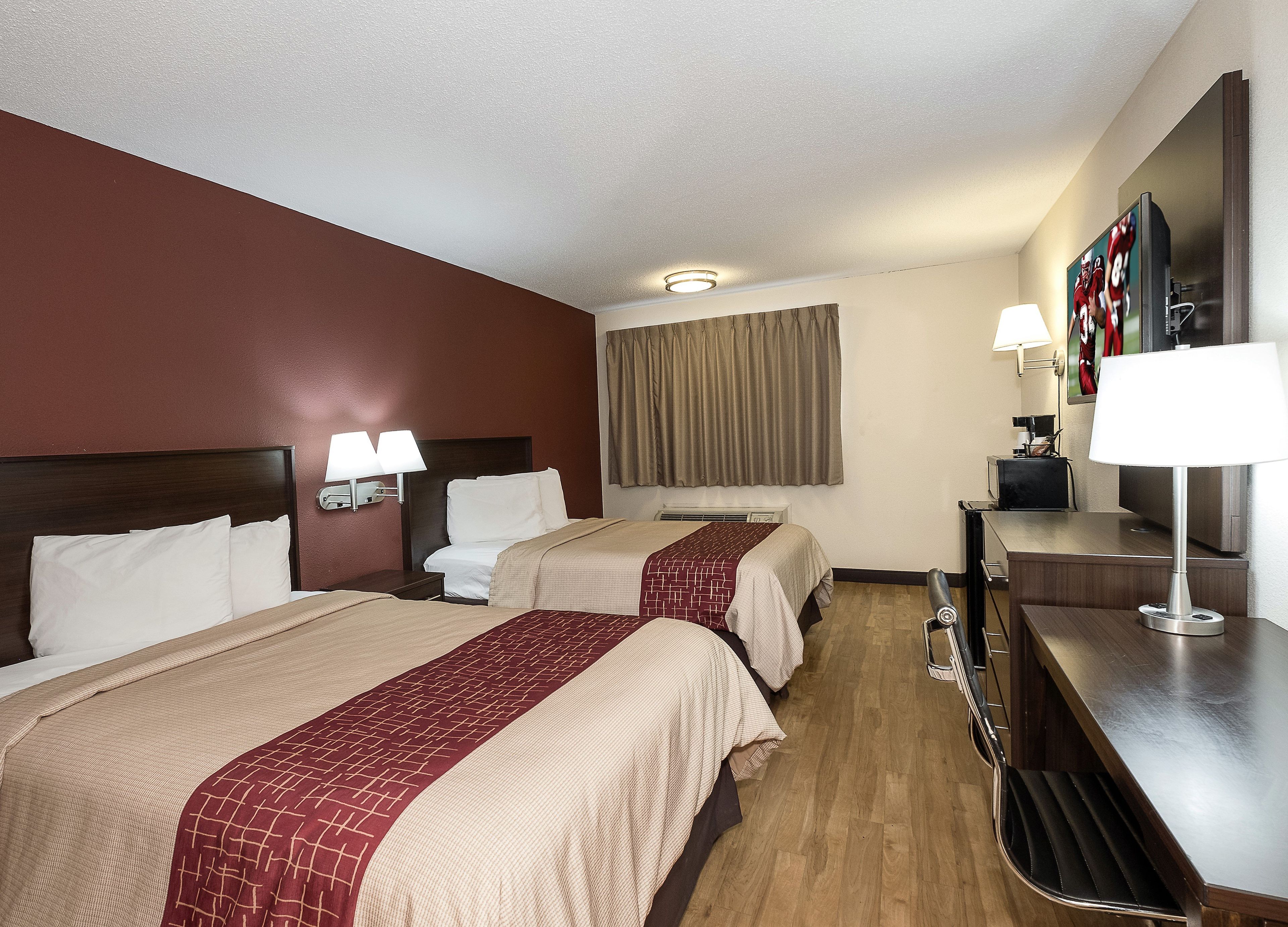 A hotel room with two beds, a desk, a television, and a window with curtains.