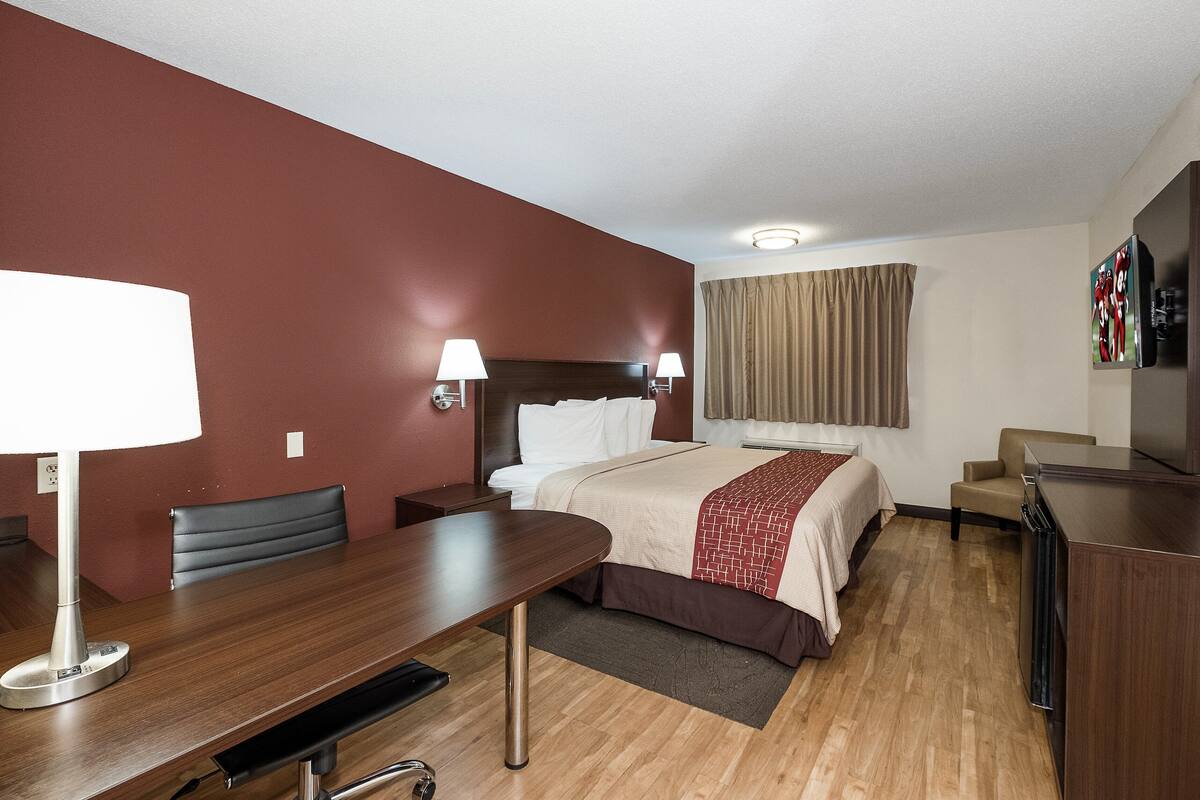A hotel room with a bed, bedside tables, a desk, a chair, a TV, and a window with curtains.