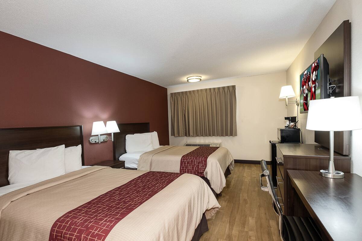 A hotel room with two beds, a desk, a TV, and a window with curtains.