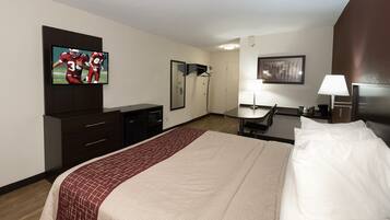 Habitación de hotel con una cama, televisor montado en la pared, escritorio con silla, espejo y lámpara.