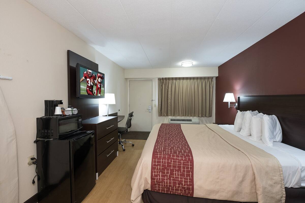 A hotel room with a bed, a desk, a microwave, a chair, and a television.