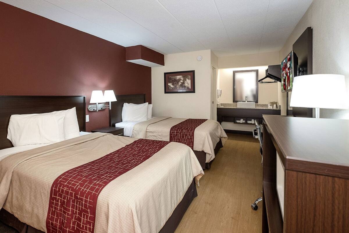 A hotel room with two beds, a desk, a mirror, and a TV.