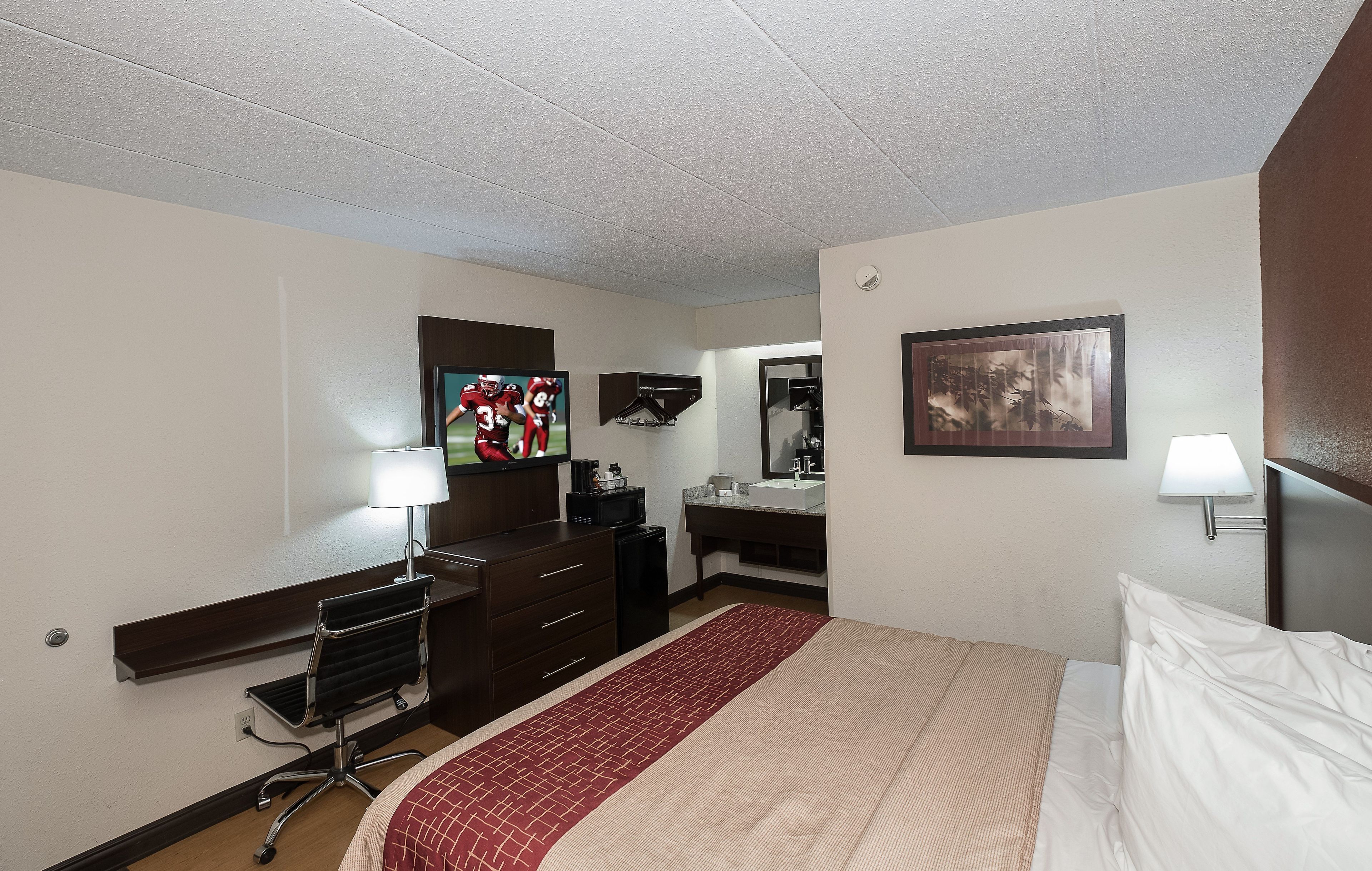 Une chambre d’hôtel comprenant un lit, un bureau avec un ordinateur, une télévision, un miroir et une salle de bain.