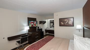 Une chambre d’hôtel comprenant un lit, un bureau avec un ordinateur, une télévision, un miroir et une salle de bain.