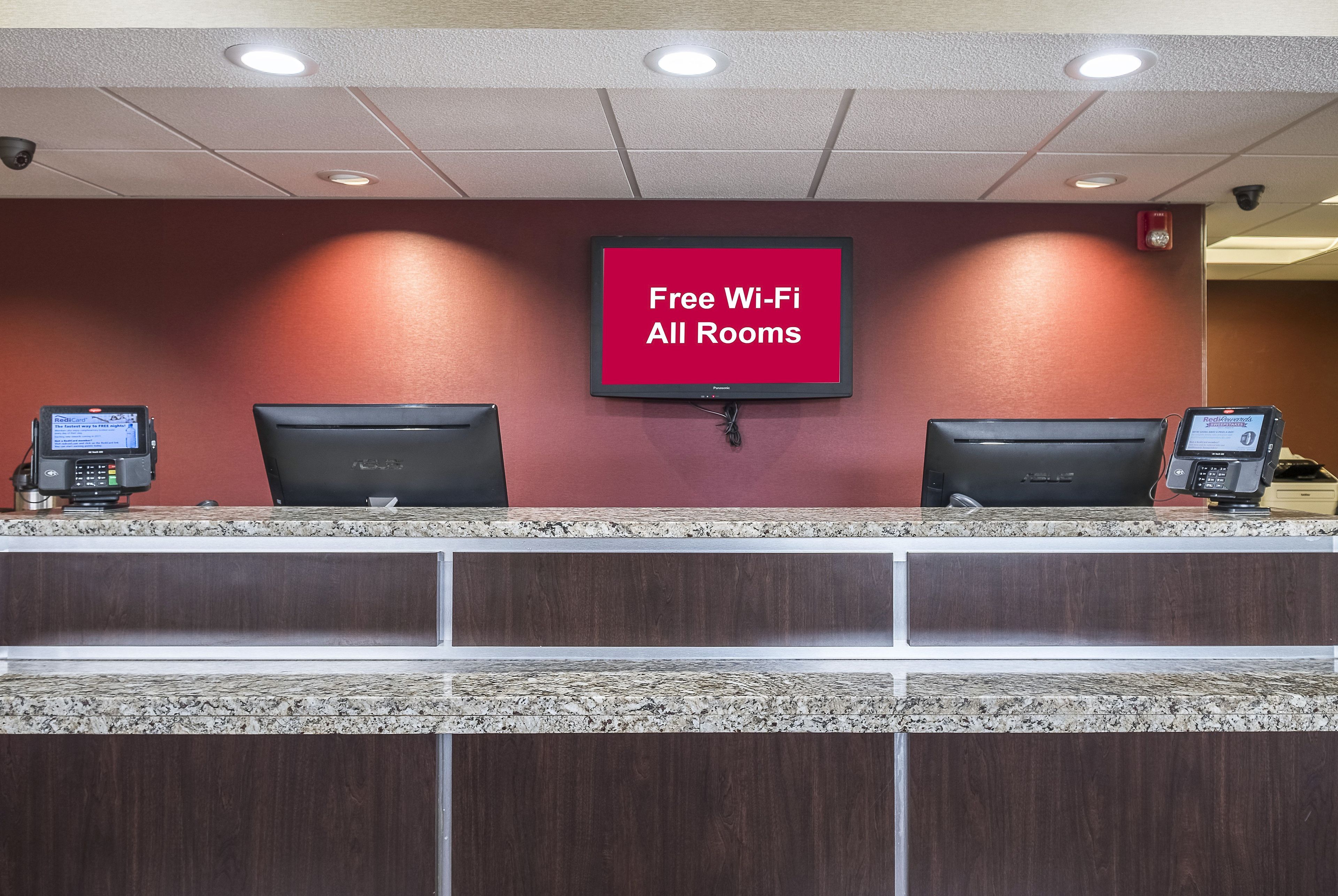 Una mesa de recepción de hotel con un televisor de pantalla plana que muestra 'Wi-Fi gratis en todas las habitaciones' y dos monitores de ordenador.