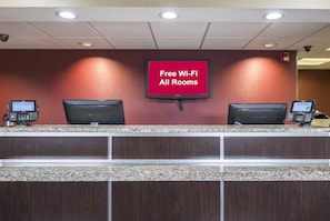 Una mesa de recepción de hotel con un televisor de pantalla plana que muestra 'Wi-Fi gratis en todas las habitaciones' y dos monitores de ordenador.