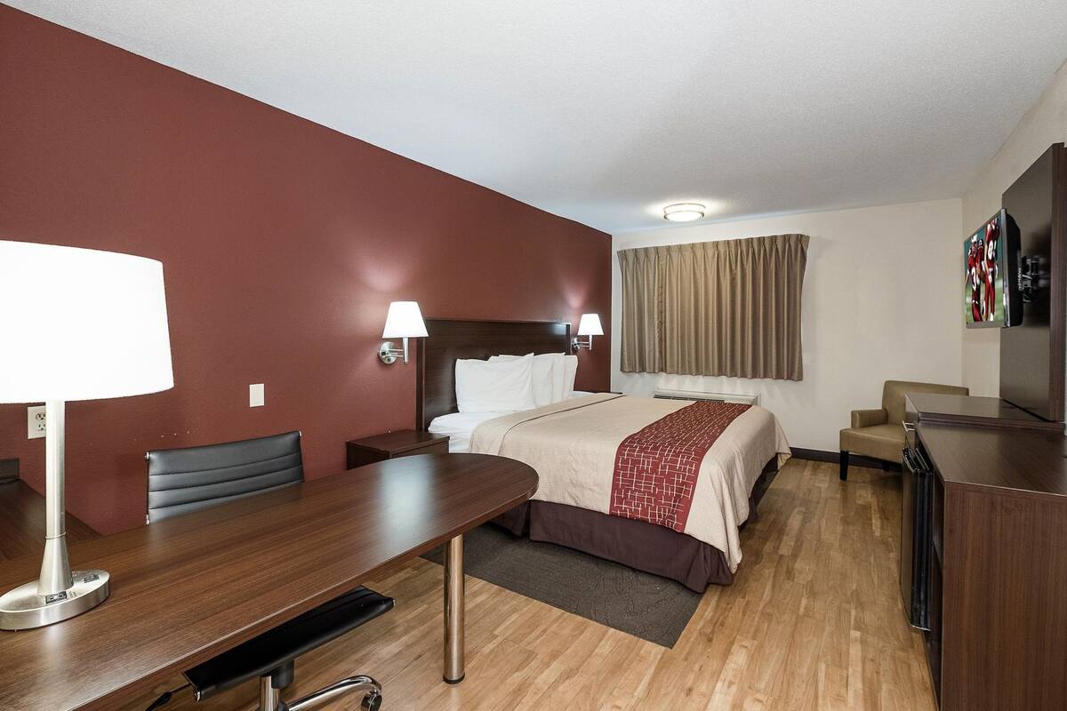 A hotel room with a bed, bedside tables, a desk, a chair, a TV, and a window with curtains.