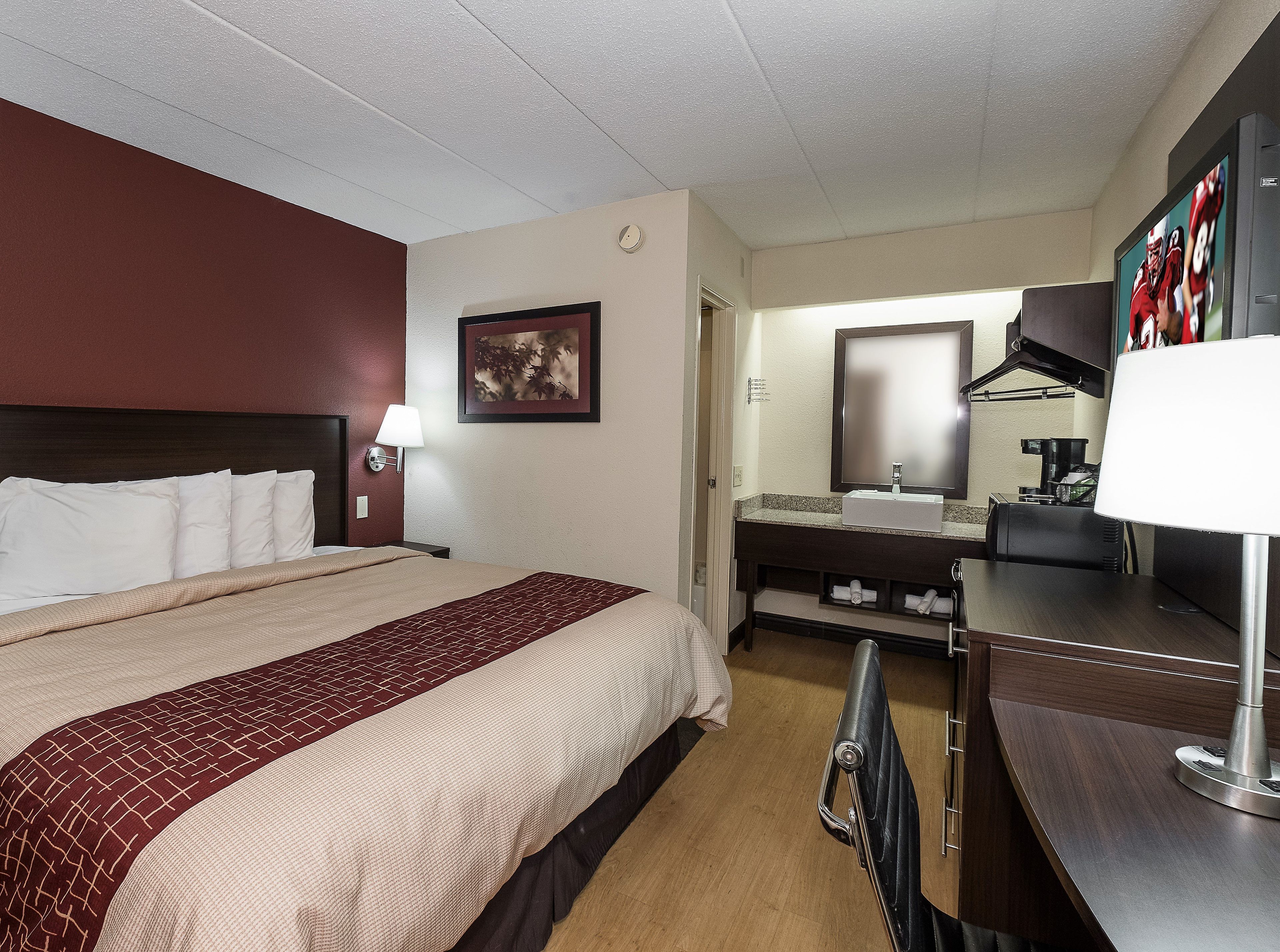 Una habitación de hotel con una cama, un escritorio, un espejo y una televisión.