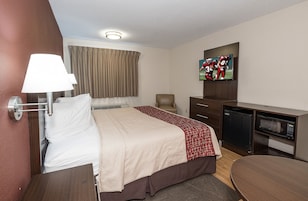Habitación de hotel con cama, escritorio, televisor, microondas y una silla.