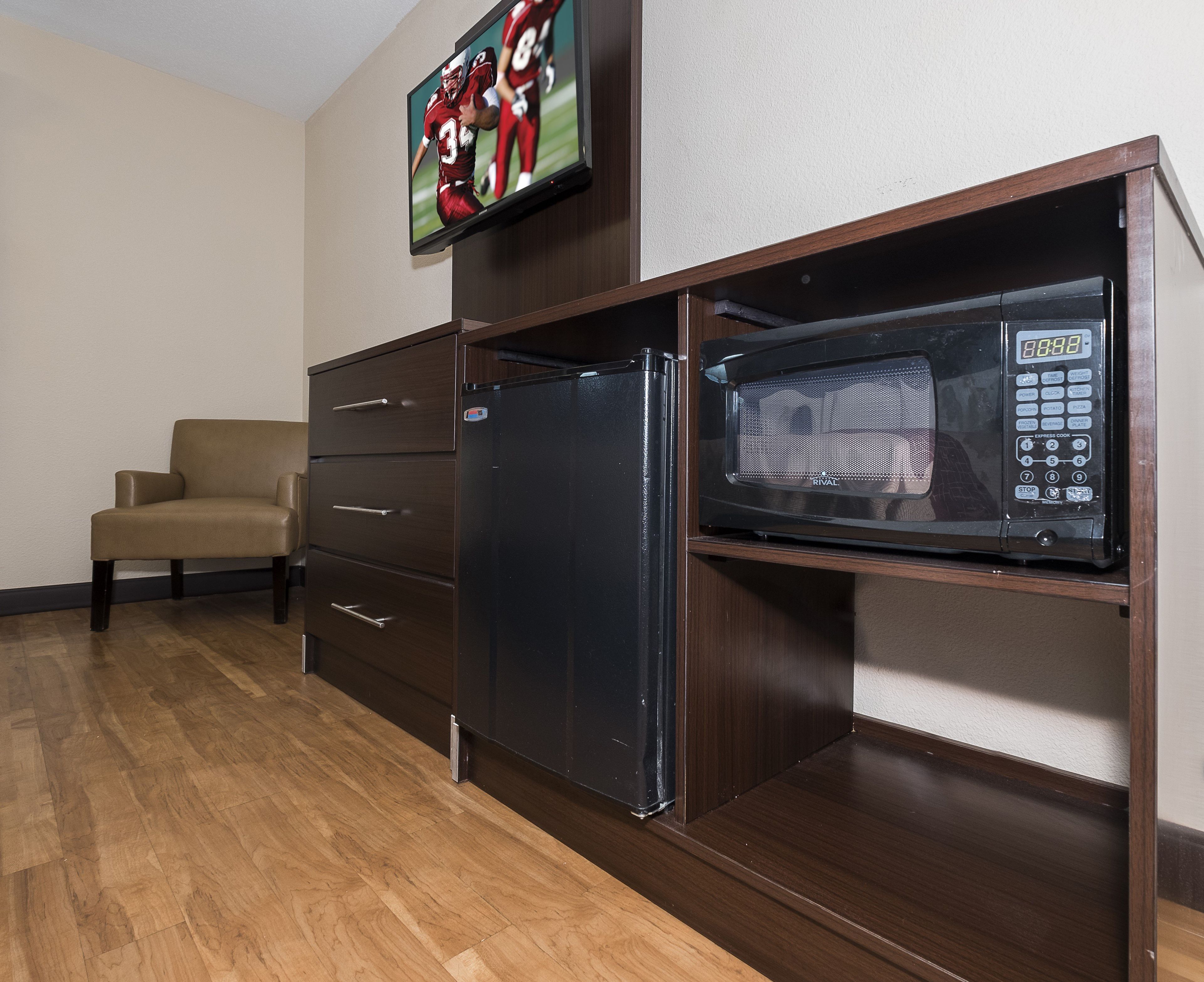 A compact kitchenette with a microwave, a refrigerator, and a television mounted above the counter.