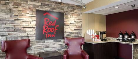 Un vestíbulo de Red Roof Inn con paredes de piedra, sillones de cuero, una estación de café y un ventilador de techo.