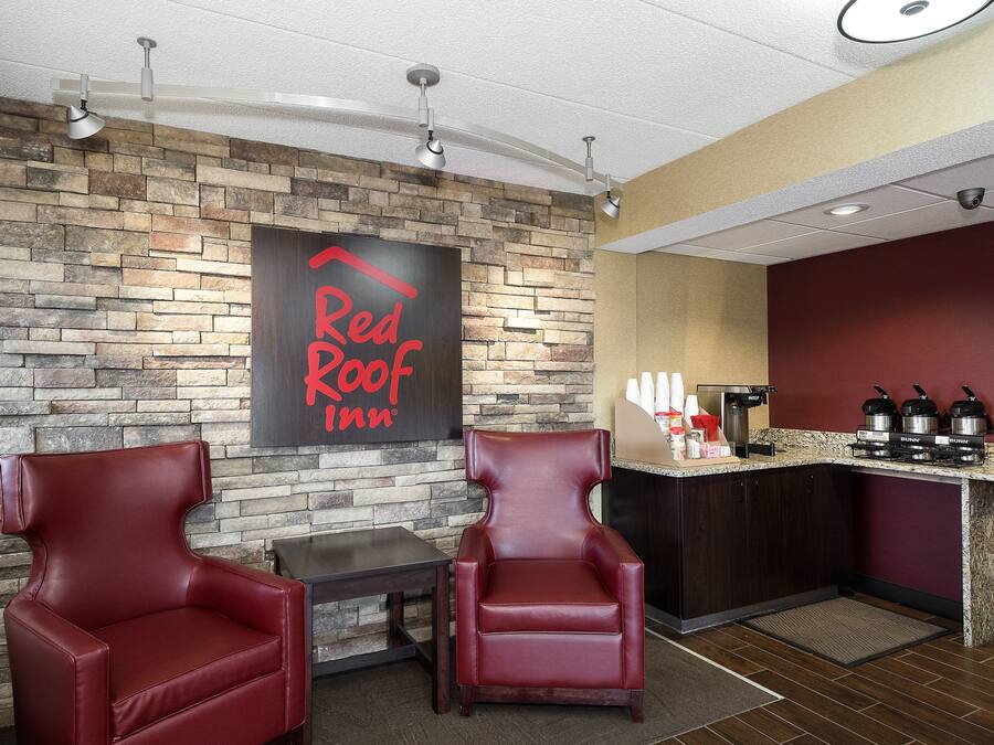Die Lobby eines Red Roof Inn mit Steinwänden, Ledersesseln, einer Kaffeestation und einem Deckenventilator.