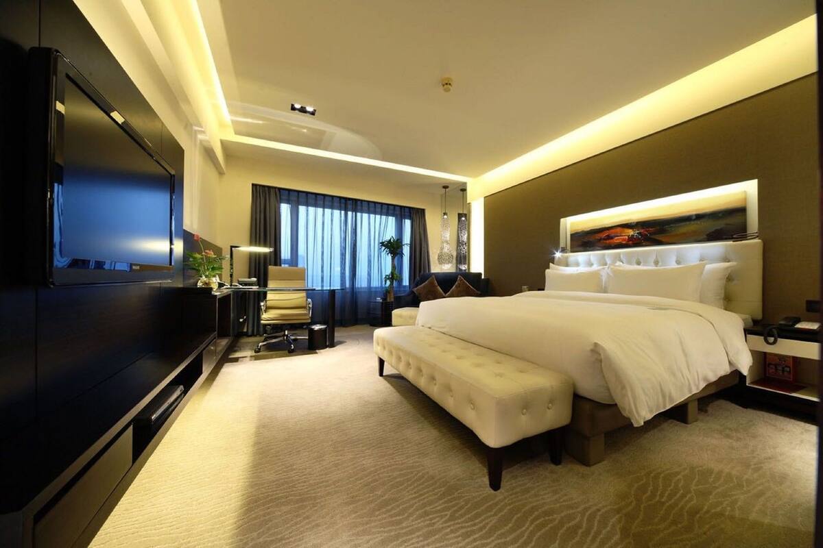 A modern hotel room with a large bed, a flat-screen TV, a desk, and a seating area.