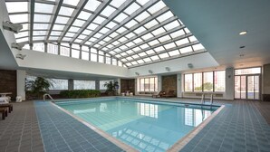 An indoor swimming pool with a high ceiling and skylights, surrounded by seating areas and a tiled floor. - Furama Hotel Dalian (Dalian)