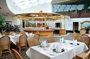 A restaurant with round tables, wicker chairs, and a central decorative structure. - Furama Hotel Dalian (Dalian)