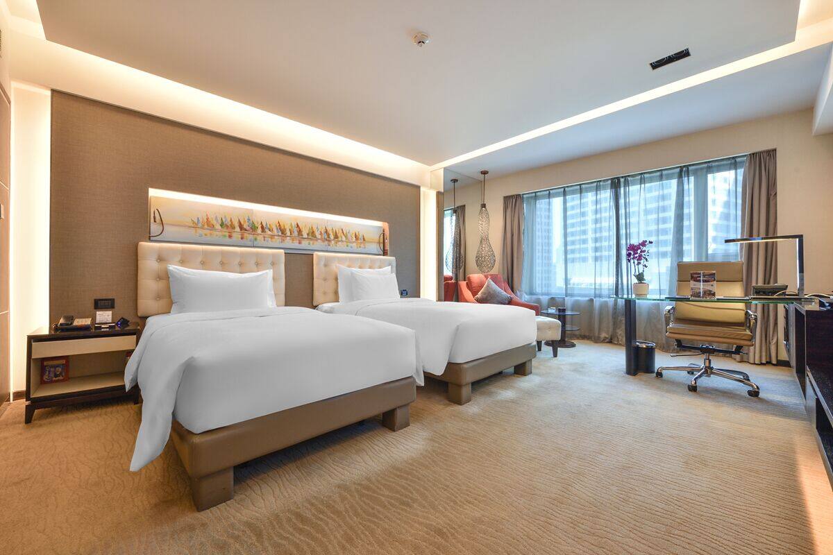A hotel room with two beds, a desk, and a large window with curtains.