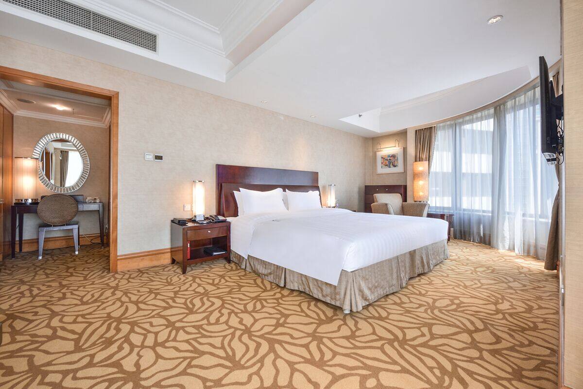 A hotel room with a large bed, a desk with a chair, a round mirror, and a television.